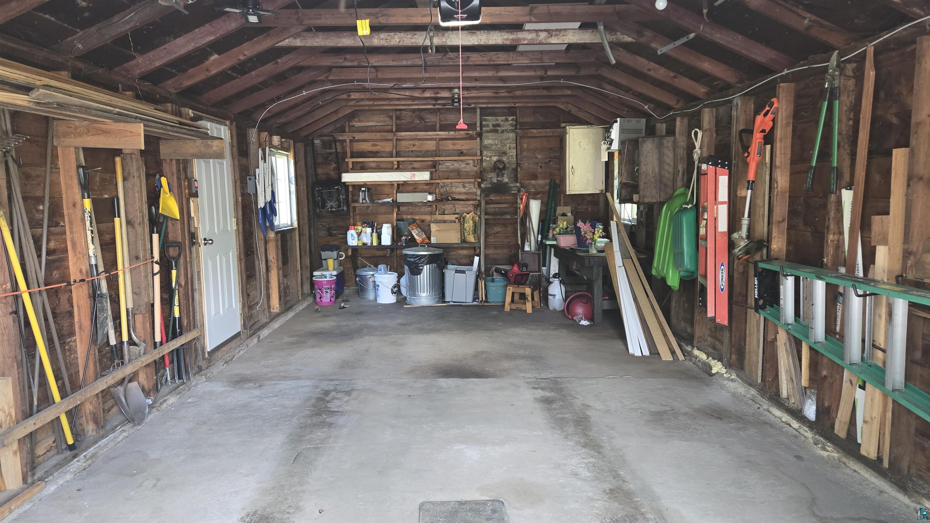 10614 Moose Lake Road Orr, MN 55771 - Photo 42 of 44 Interior garage space featuring exposed wood framing, concrete flooring, built-in shelving, and a side access door