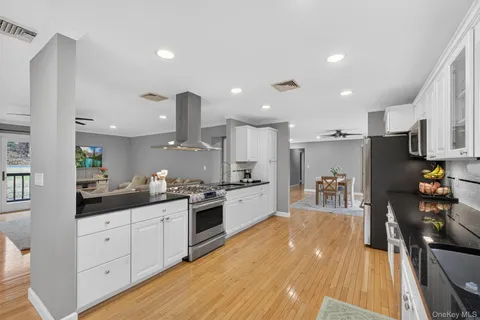 a kitchen with stainless steel appliances kitchen island granite countertop a stove top oven a sink a dining table and chairs with wooden floor