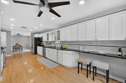 a kitchen with stainless steel appliances granite countertop a sink a stove top oven a refrigerator with white cabinets and wooden floor