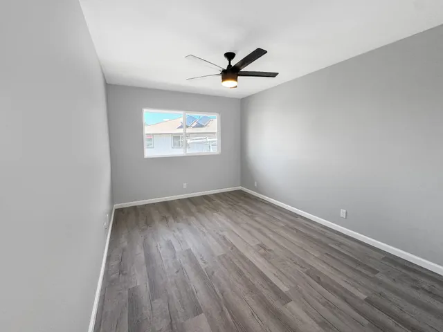 an empty room with wooden floor ceiling fan and windows