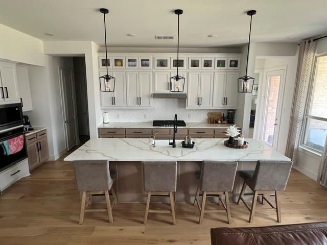 1407 Cartona Road Fate, TX 75087 - Photo 14 of 30 Gourmet kitchen featuring a large central island with seating, a herringbone tile backsplash, white upper cabinetry, and contrasting wood-finish lower cabinetry