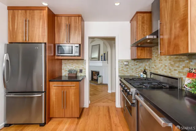 a kitchen with stainless steel appliances granite countertop a refrigerator a stove and a sink with wooden floor