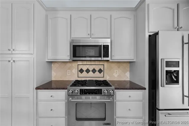 a kitchen with stainless steel appliances granite countertop white cabinets and a stove a refrigerator with white cabinets