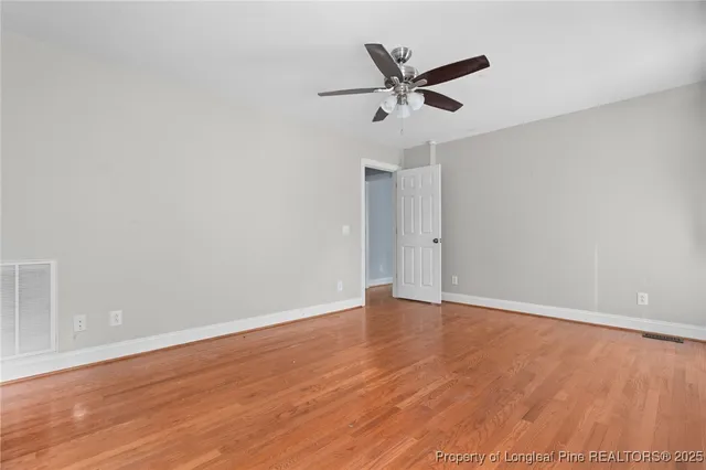 an empty room with wooden floor fan and windows