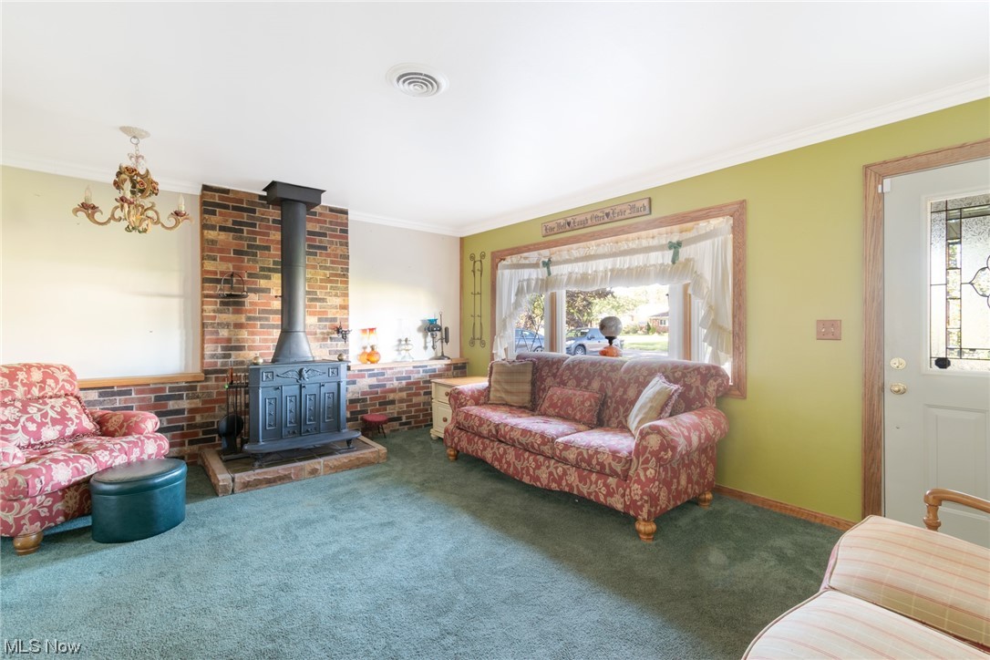 Carpeted living room with a wealth of natural light, ornamental molding, brick wall, and a fireplace