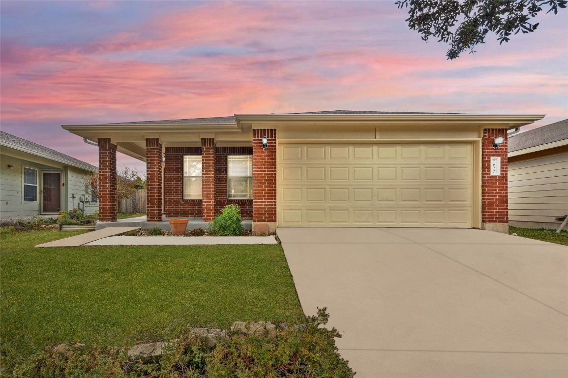 View of front of house with concrete driveway, brick siding, covered porch, an attached garage, and a lawn