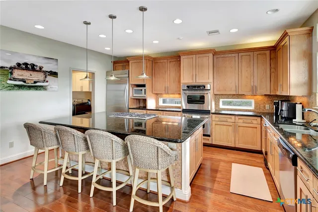 a kitchen with stainless steel appliances granite countertop a refrigerator a sink dishwasher a stove and a dining table with wooden floor