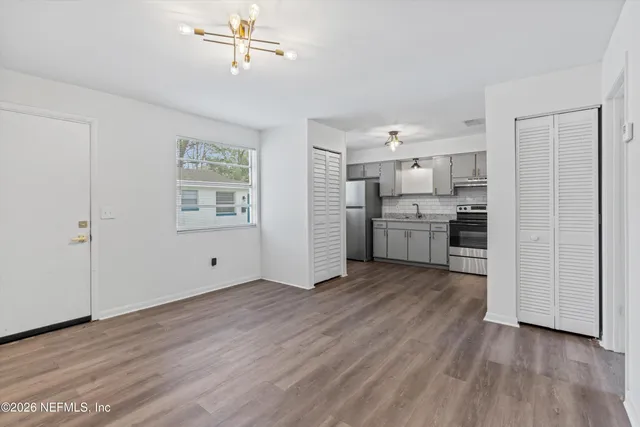 an empty room with wooden floor kitchen view and a window