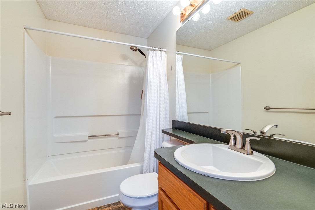 5303 Laubert Road Atwater, OH 44201 - Photo 30 of 37 Full bathroom featuring shower / bath combination with curtain, oversized vanity, toilet, and a textured ceiling