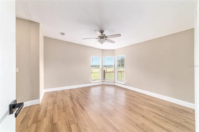an empty room with wooden floor fan and windows