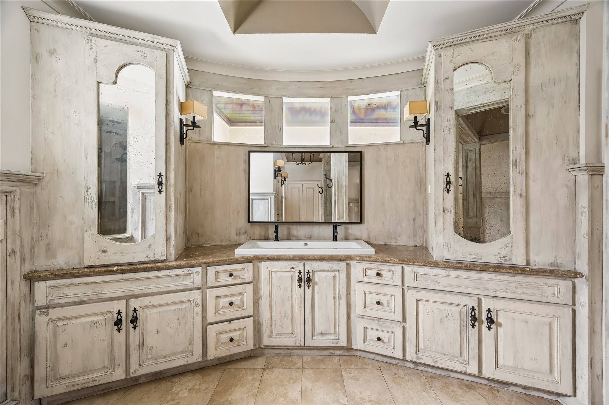 2246 Branard Street Houston, TX 77098 - Photo 29 of 40 Custom dual vanities with extensive storage and distressed cabinetry are framed by soft natural light and warm stone surfaces, creating a refined, old-world feel.