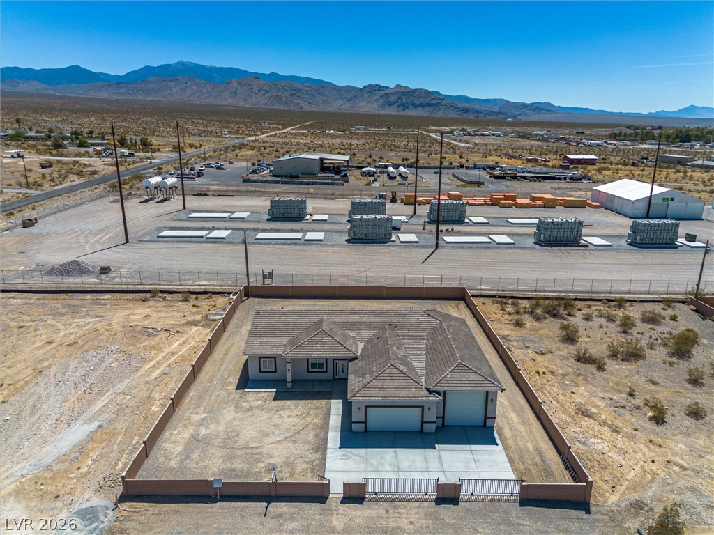 1061 Factory Road Pahrump, NV 89048 - Photo 37 of 41 An aerial perspective reveals a desert home with a paved driveway and an enclosed yard, set against a mountain backdrop.