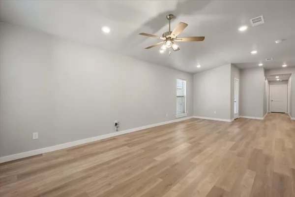 a view of an empty room with wooden floor and fan