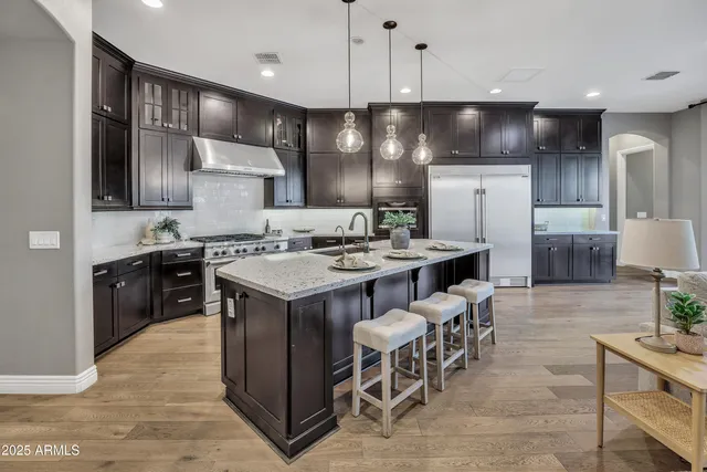 a kitchen with stainless steel appliances kitchen island granite countertop a stove a refrigerator a sink a dining table and chairs with wooden floor