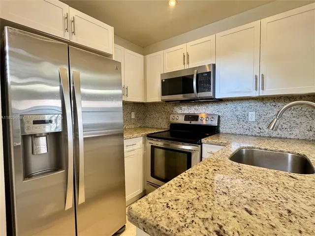 a kitchen with stainless steel appliances granite countertop a refrigerator a stove and a sink with wooden floor