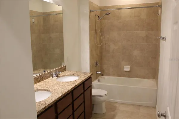 a bathroom with a granite countertop bathtub shower sink vanity and toilet
