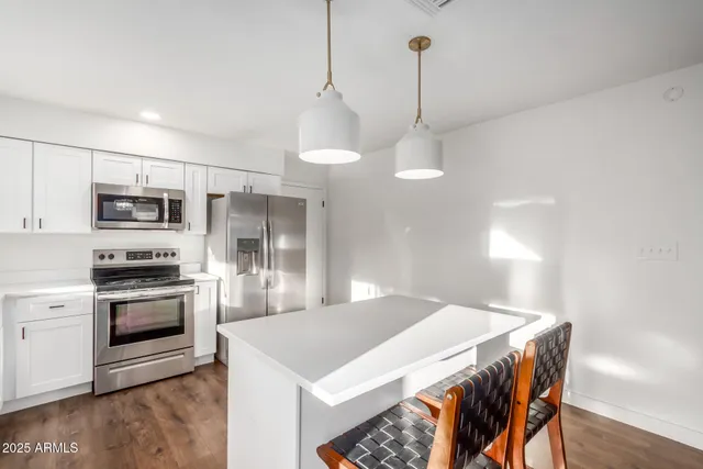 a kitchen with stainless steel appliances a stove a sink island a refrigerator and a wooden floor