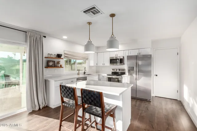 a kitchen with stainless steel appliances kitchen island granite countertop a refrigerator a stove and a wooden floors