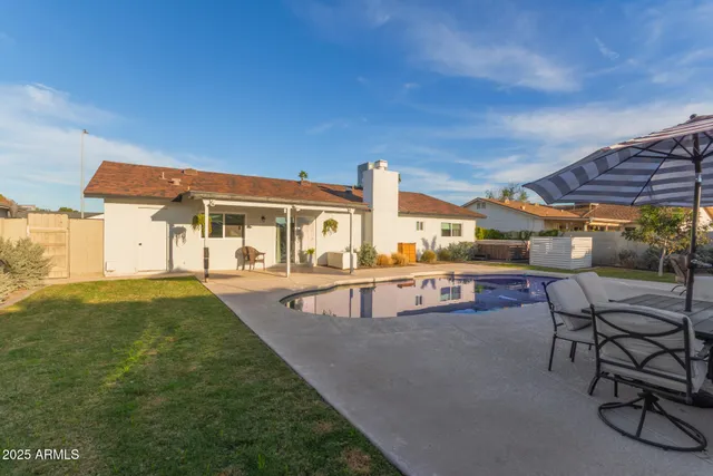 a view of a patio with dining table and chairs under an umbrella with large trees