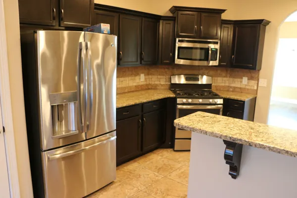 a kitchen with granite countertop a refrigerator stove microwave and sink