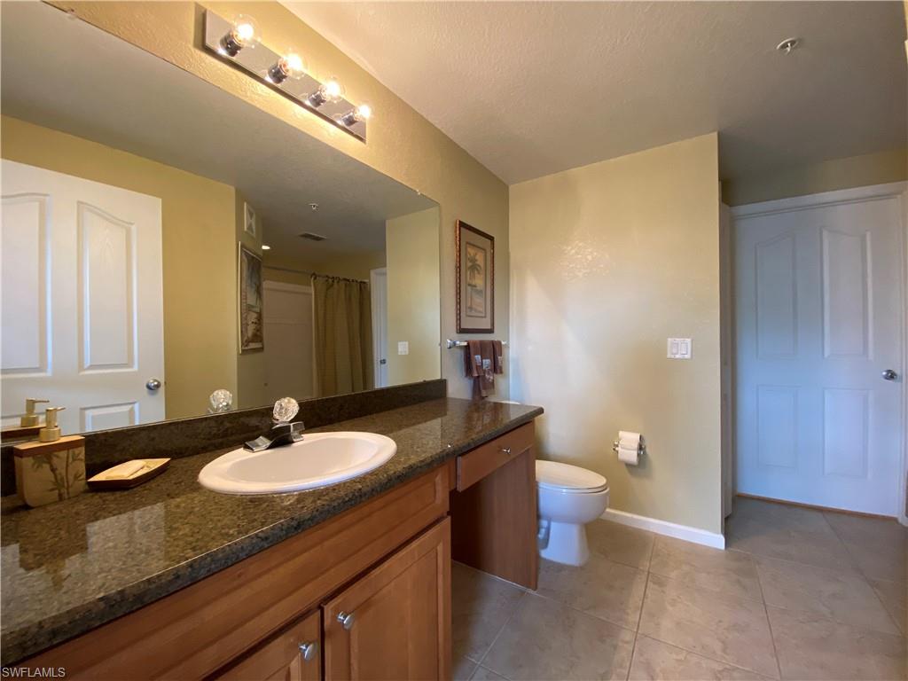 12940 Positano Circle, Unit 204 Naples, FL 34105 - Photo 19 of 39 a bathroom with a granite countertop sink a toilet a mirror and shower