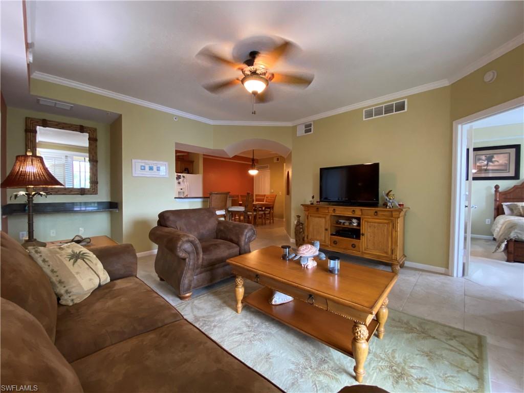 12940 Positano Circle, Unit 204 Naples, FL 34105 - Photo 8 of 39 a living room with furniture a chandelier and a flat screen tv