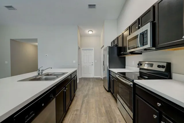 a kitchen with stainless steel appliances a sink dishwasher stove top oven and wooden floor