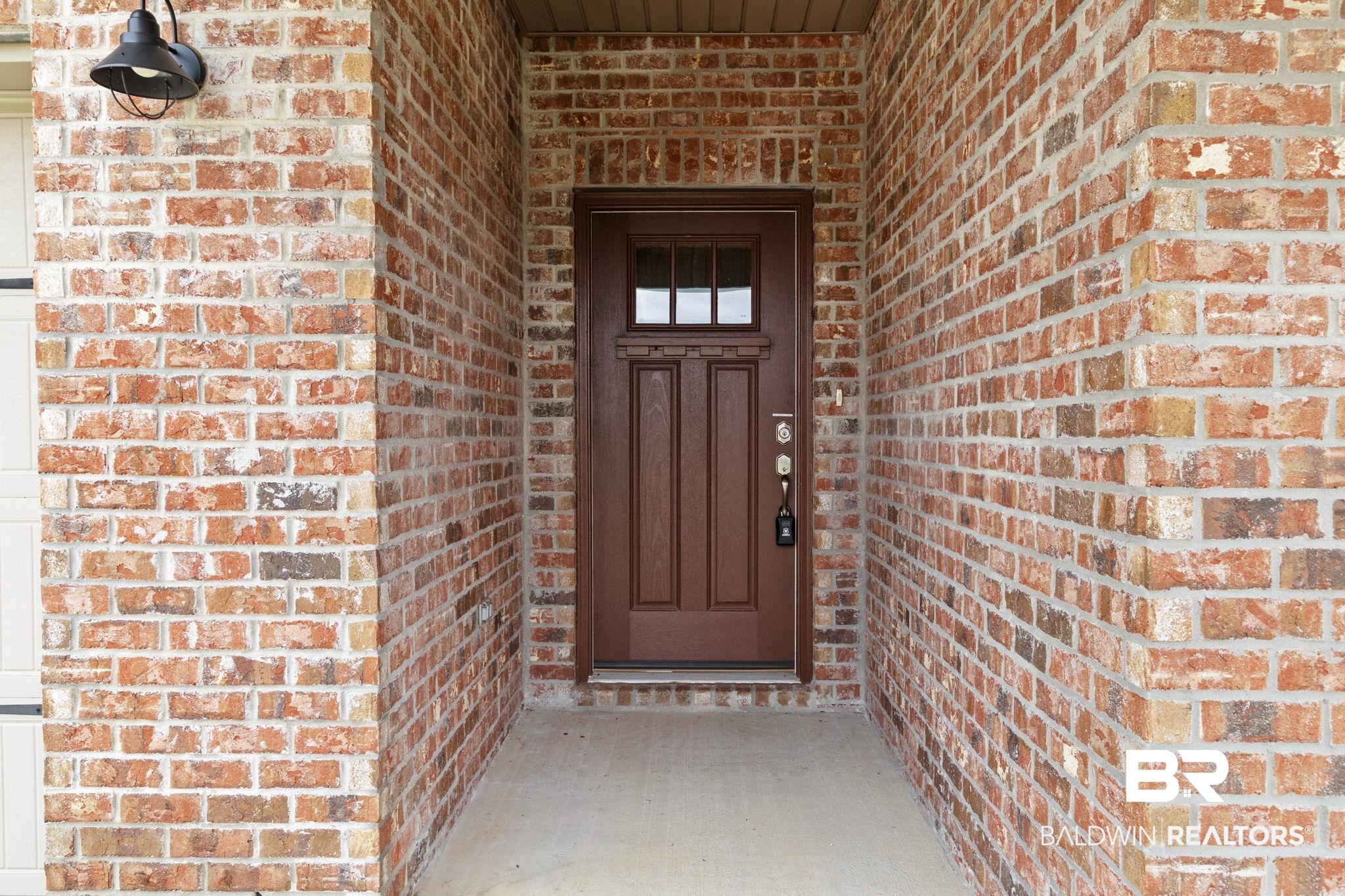 1710 Grouse Street Foley, AL 36535 - Photo 13 of 76 Brick exterior featuring a paneled entry door with glass inserts, a single exterior light fixture, and concrete walkway