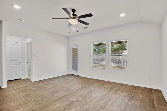 an empty room with wooden floor fan and windows