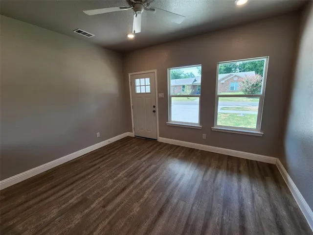 an empty room with wooden floor chandelier fan and windows