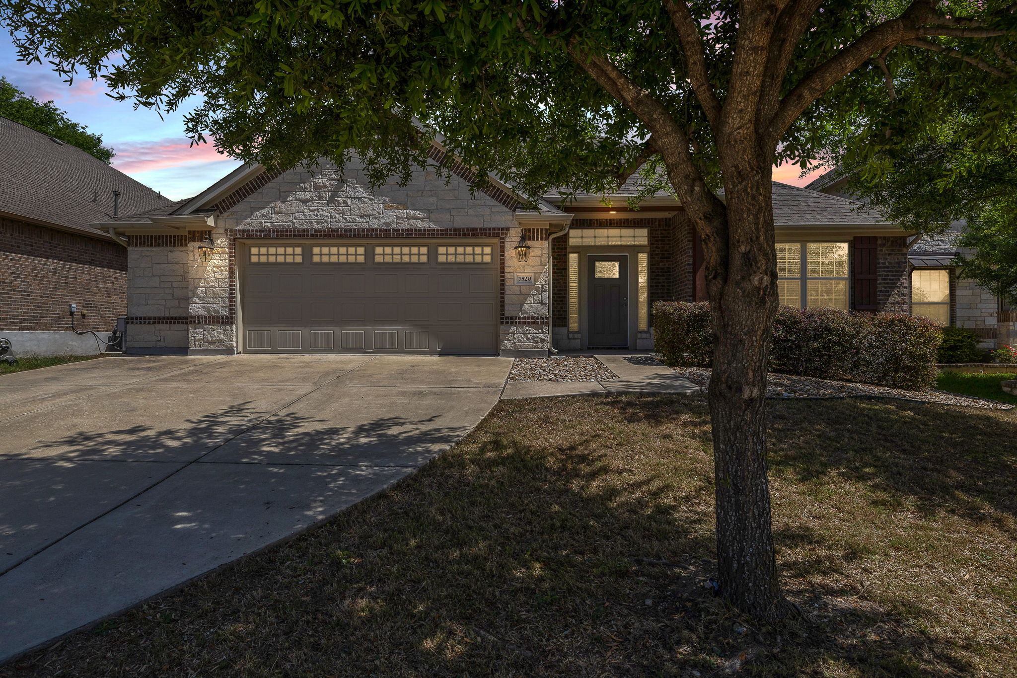Ranch-style home featuring an attached garage, concrete driveway, stone siding, and a yard