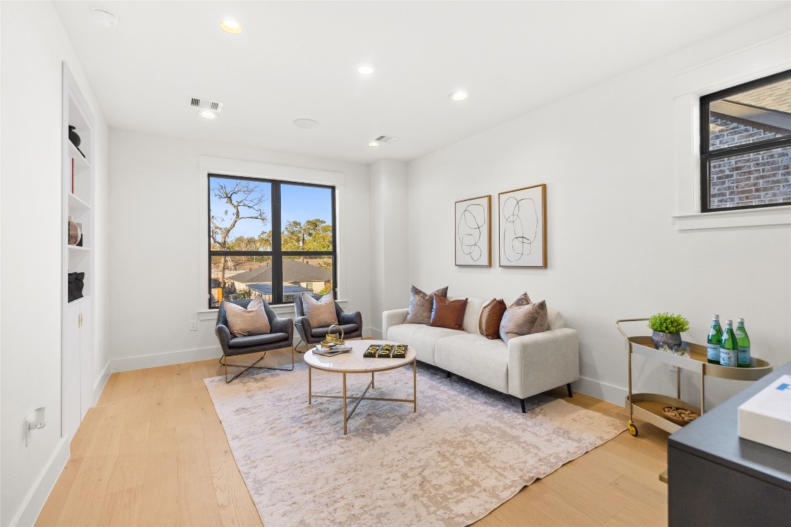 7115 Raton Street Houston, TX 77055 - Photo 16 of 49 This is where your everyday living feels elevated—clean white walls, wide-plank wood floors, and oversized windows that pull in natural light all day long. The layout is perfectly scaled for comfortable seating without wasting space, making it easy to relax, entertain, or unwind at the end of the day. Tucked along the left side, a seamless Murphy door blends into the wall, offering a hidden entry that adds both function and a touch of architectural intrigue without interrupting the room’s clean lines.