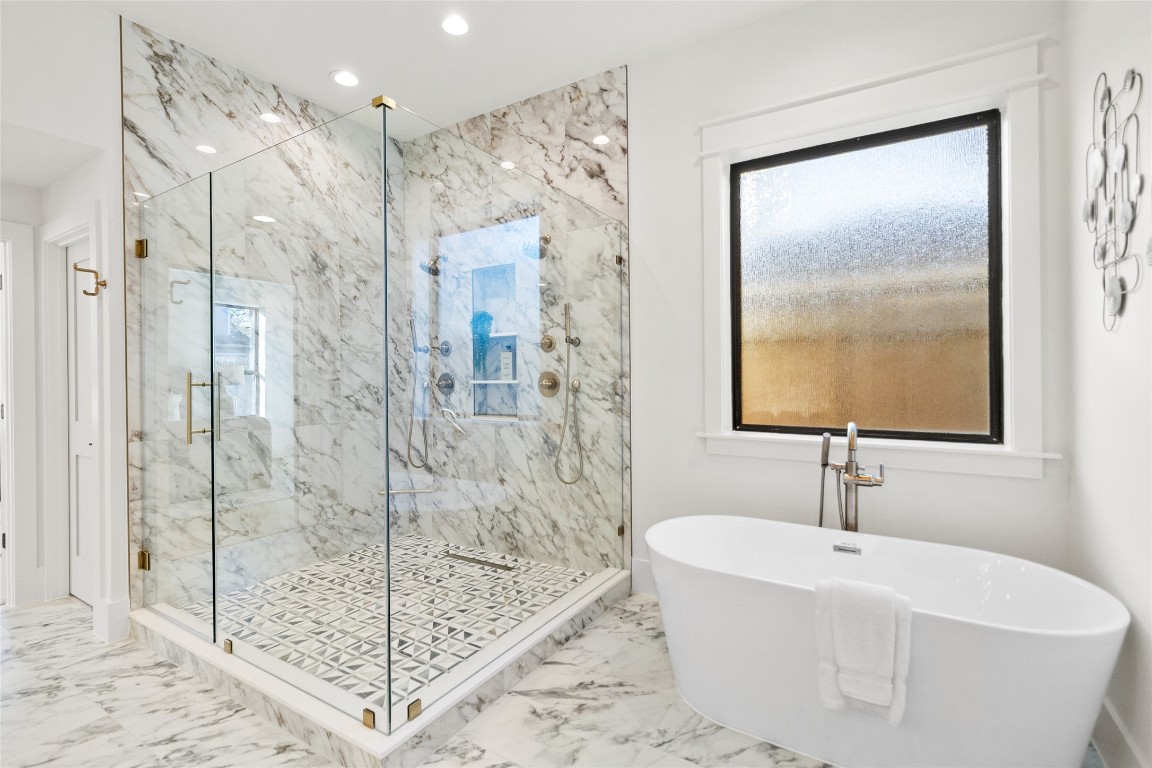 7115 Raton Street Houston, TX 77055 - Photo 25 of 49 This primary bath is your personal sanctuary—an oversized glass-enclosed shower with statement marble tile sits alongside a sculptural freestanding soaking tub beneath a frosted window. Patterned flooring, refined fixtures, and abundant natural light create a calm, high-end space designed for unwinding in style.
