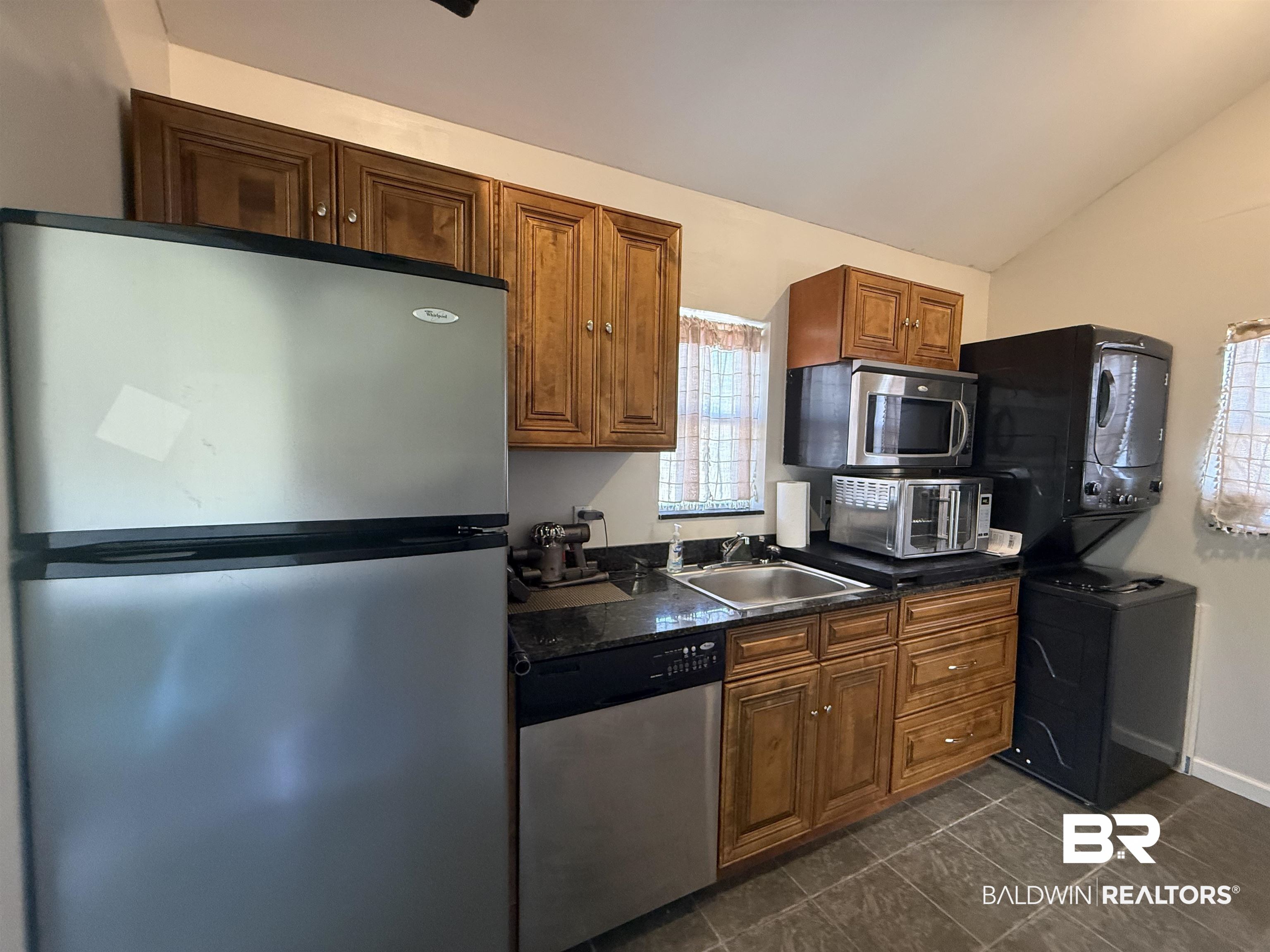 28114 Preserve Trail, Unit 190 Elberta, AL 36530 - Photo 29 of 69 Kitchen featuring stainless steel appliances, wood finish cabinets, lofted ceiling, dark tile patterned flooring, and dark stone counters