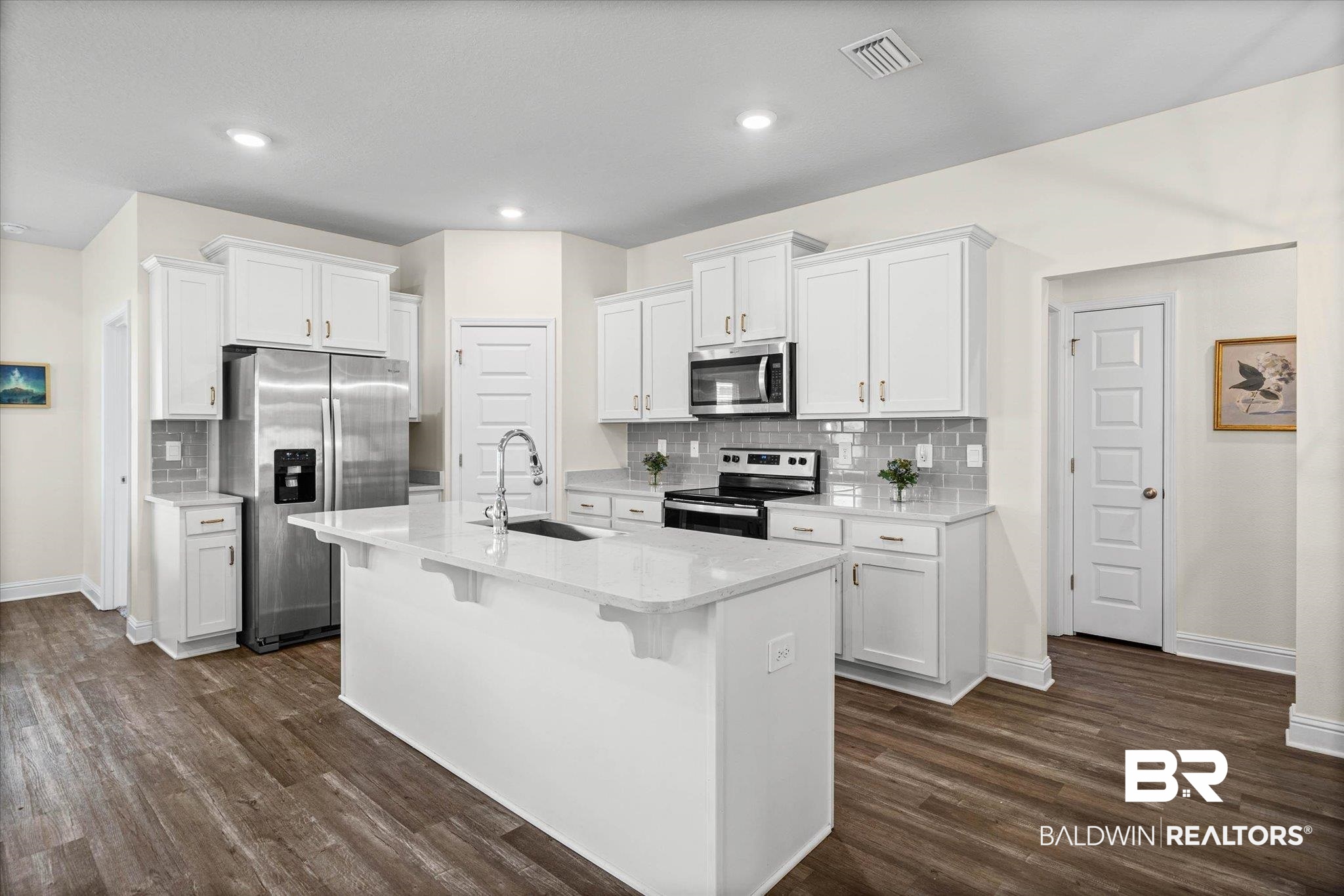 10541 Heirloom Road South Mobile, AL 36608 - Photo 7 of 23 Contemporary kitchen featuring a large central island with an undermount sink, white cabinetry with crown molding, stainless steel appliances, and wood-finish flooring