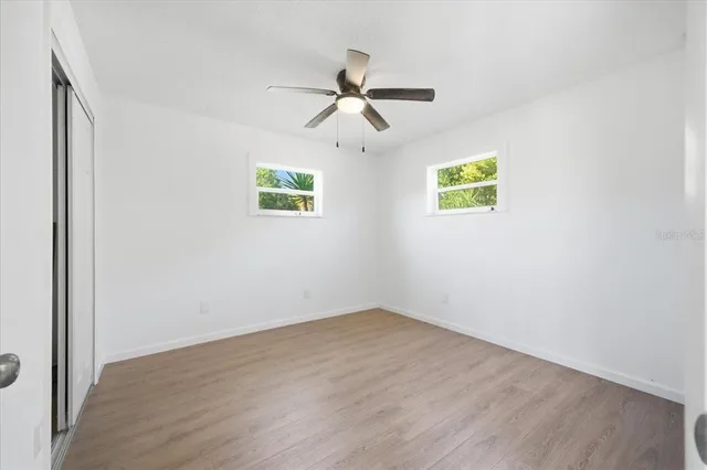 an empty room with wooden floor ceiling fan and windows