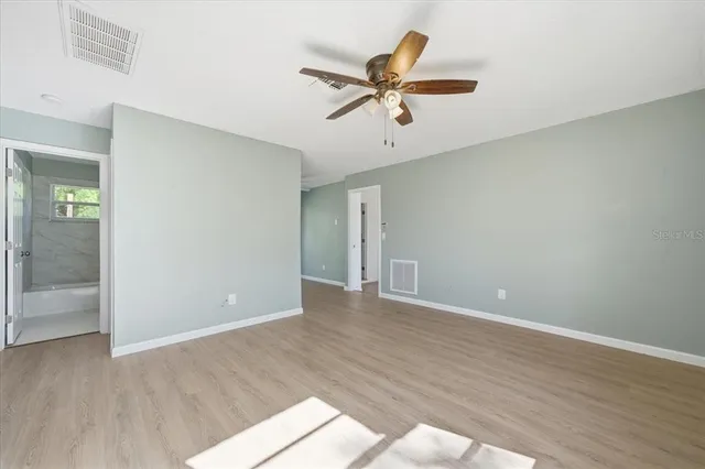 an empty room with wooden floor fan and windows