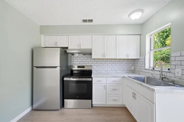 a kitchen with white cabinets white stainless steel appliances and window