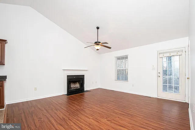 a view of an empty room with wooden floor fireplace and a window