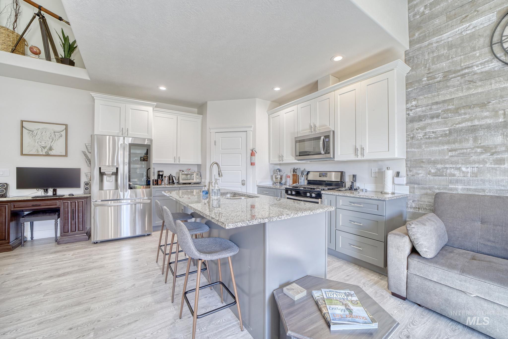 1087 Easy Avenue Twin Falls, ID 83301 - Photo 7 of 25 Kitchen with appliances with stainless steel finishes, white cabinetry, a breakfast bar, light stone counters, and light wood-type flooring