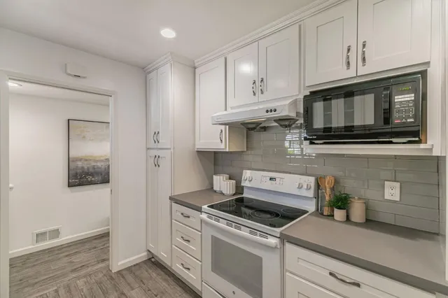 a kitchen with stainless steel appliances granite countertop white cabinets a stove a sink and dishwasher
