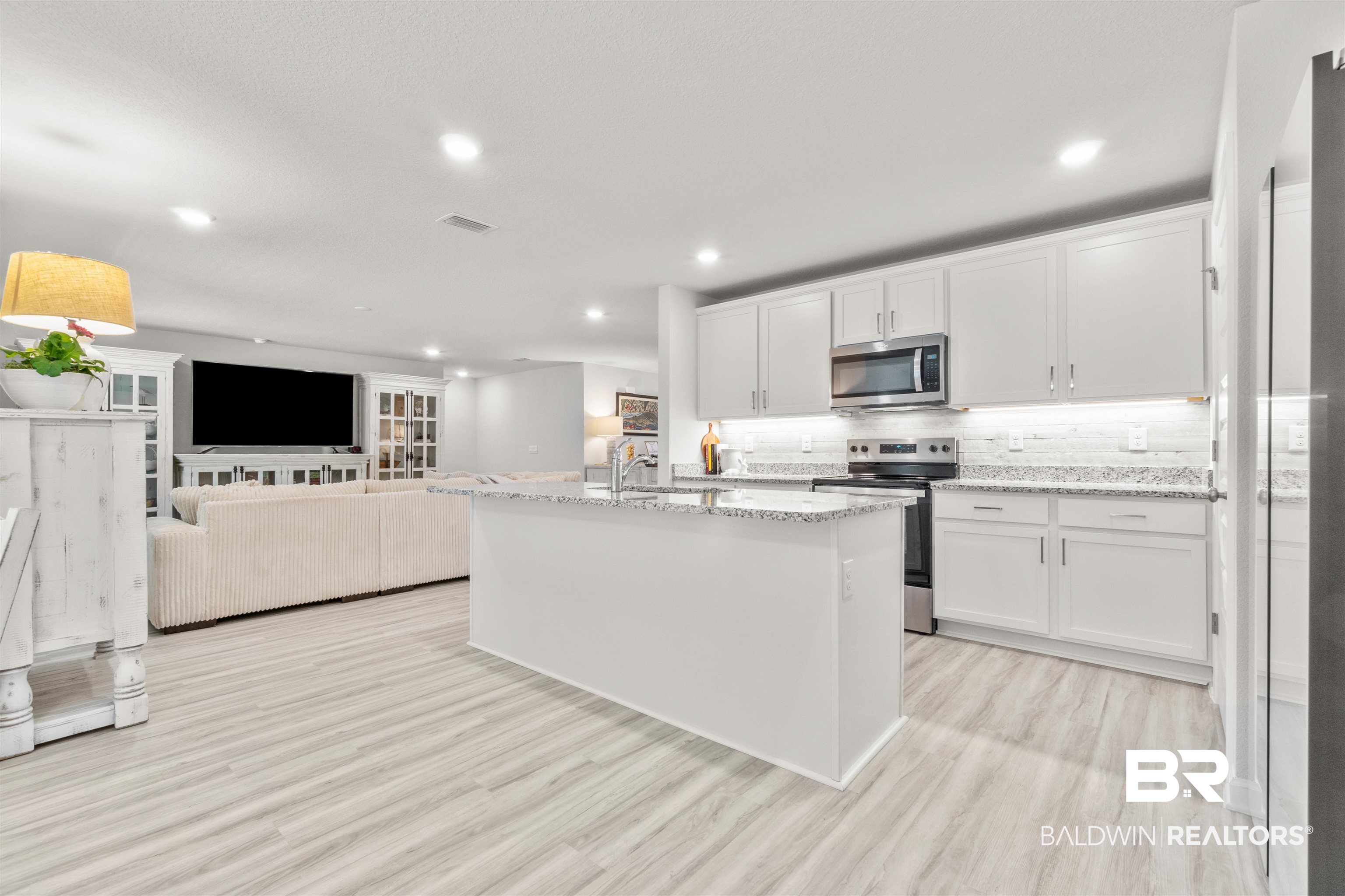 24472 Ringneck Loop Elberta, AL 36530 - Photo 10 of 46 Kitchen with appliances with stainless steel finishes, light hardwood / wood-style floors, white cabinets, an island with sink, and light stone countertops