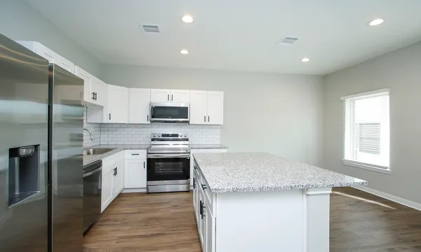 a kitchen with stainless steel appliances white cabinets a sink a stove a microwave and wooden floor