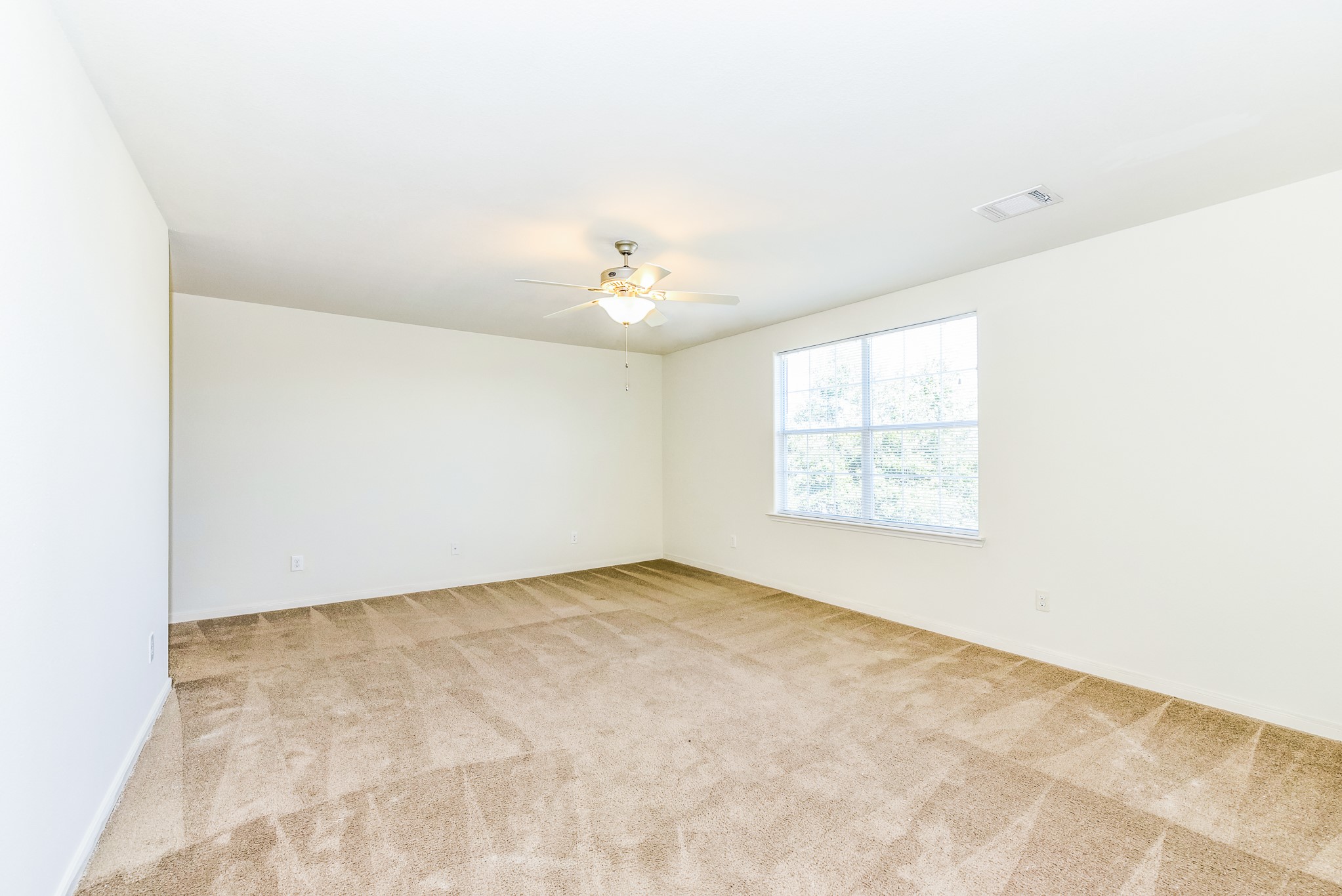 28854 Llano River Loop Spring, TX 77386 - Photo 12 of 19 This photo shows a spacious, carpeted Primary Bedroom with neutral walls, a large window letting in natural light, and a ceiling fan with a light fixture.