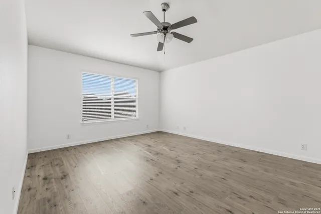 an empty room with wooden floor ceiling fan and windows