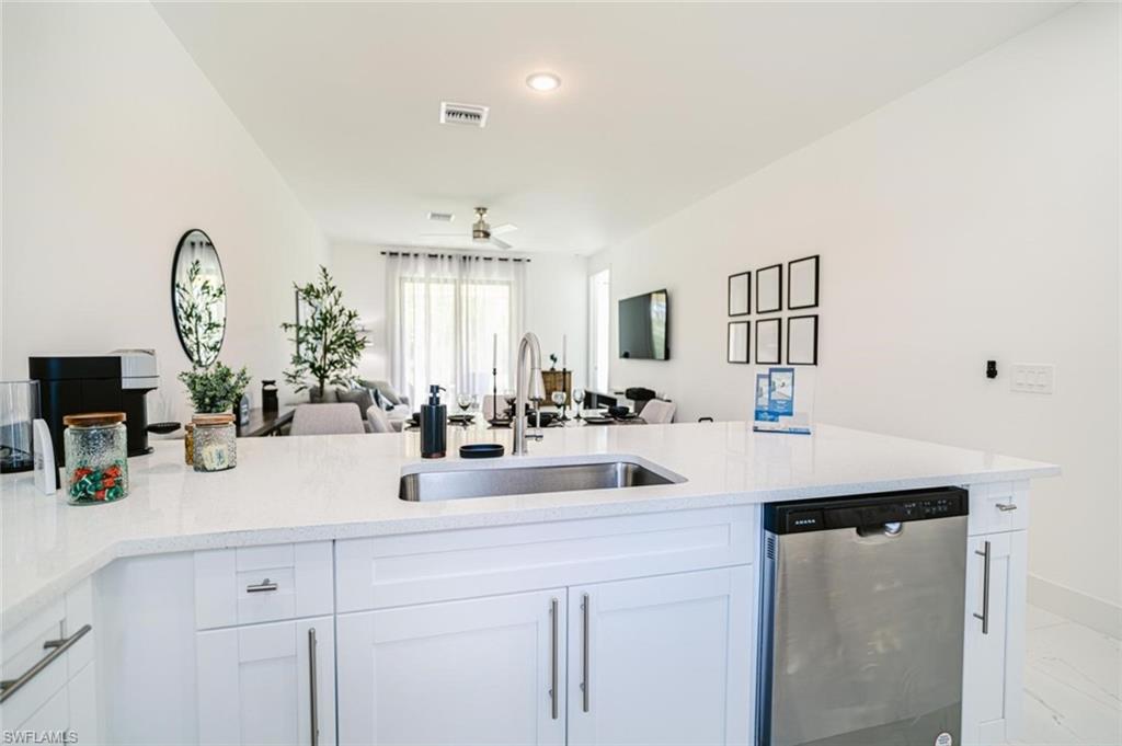907 Homestead Road South Lehigh Acres, FL 33974 - Photo 7 of 43 Kitchen island with a stainless steel undermount sink, a gooseneck faucet, white cabinetry, and a built-in stainless steel dishwasher