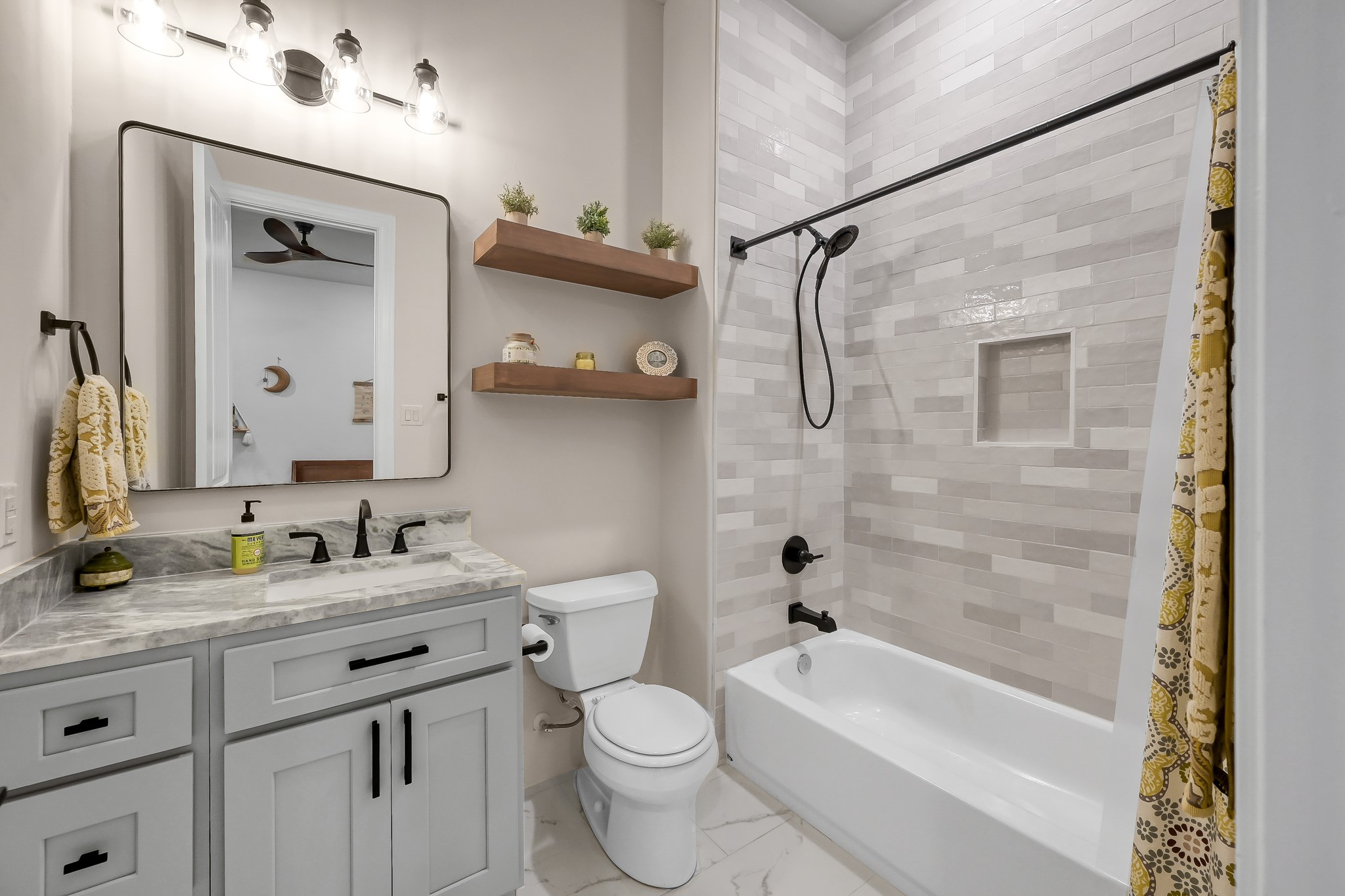 15937 Stagecoach Road Stagecoach, TX 77355 - Photo 27 of 50 This bathroom features a modern design with a sleek vanity and marble countertop. It has a bathtub with a to the ceiling tile and black fixtures. Open shelving adds a touch of warmth, while the lighting above the mirror enhances the space.