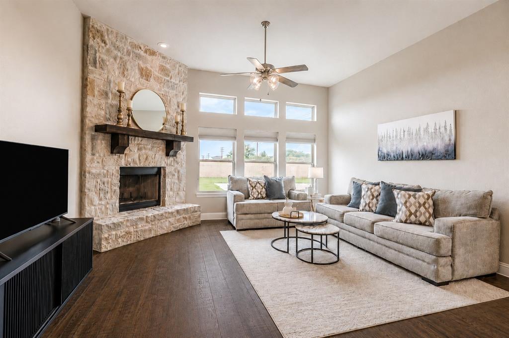 25 Morrison Road Howe, TX 75459 - Photo 3 of 27 Living space featuring a stone-clad fireplace with a wood mantel, high ceilings, wood-finish flooring, a ceiling fan with integrated lighting, and multiple windows
