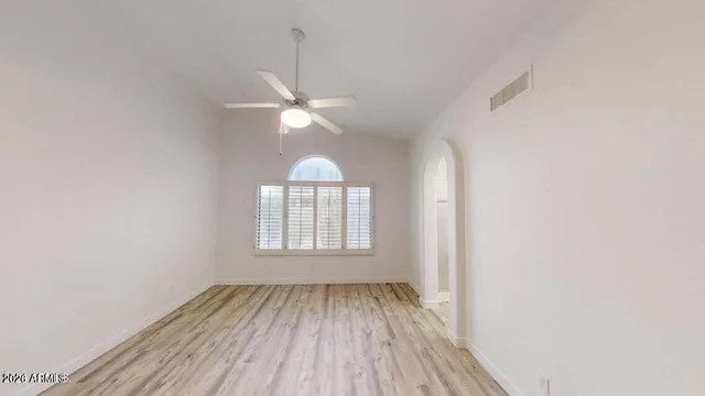 an empty room with wooden floor fan and windows