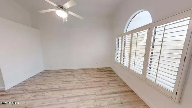 an empty room with wooden floor fan and windows